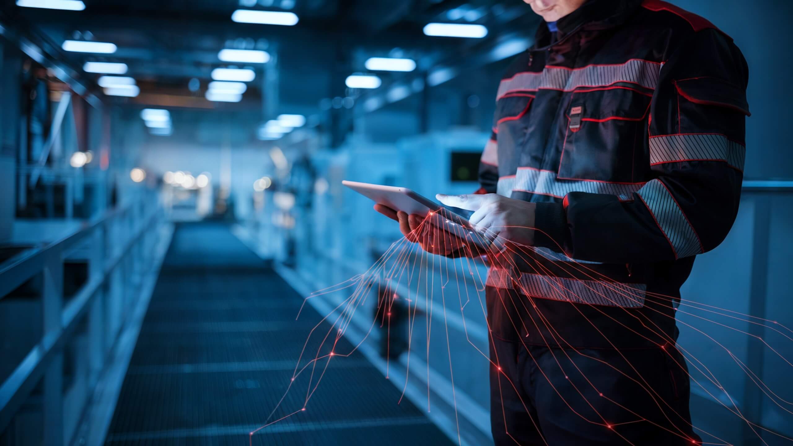 Technician in protective clothing operating a tablet in a modern industrial facility, surrounded by red data lines symbolizing digital processes and connectivity.