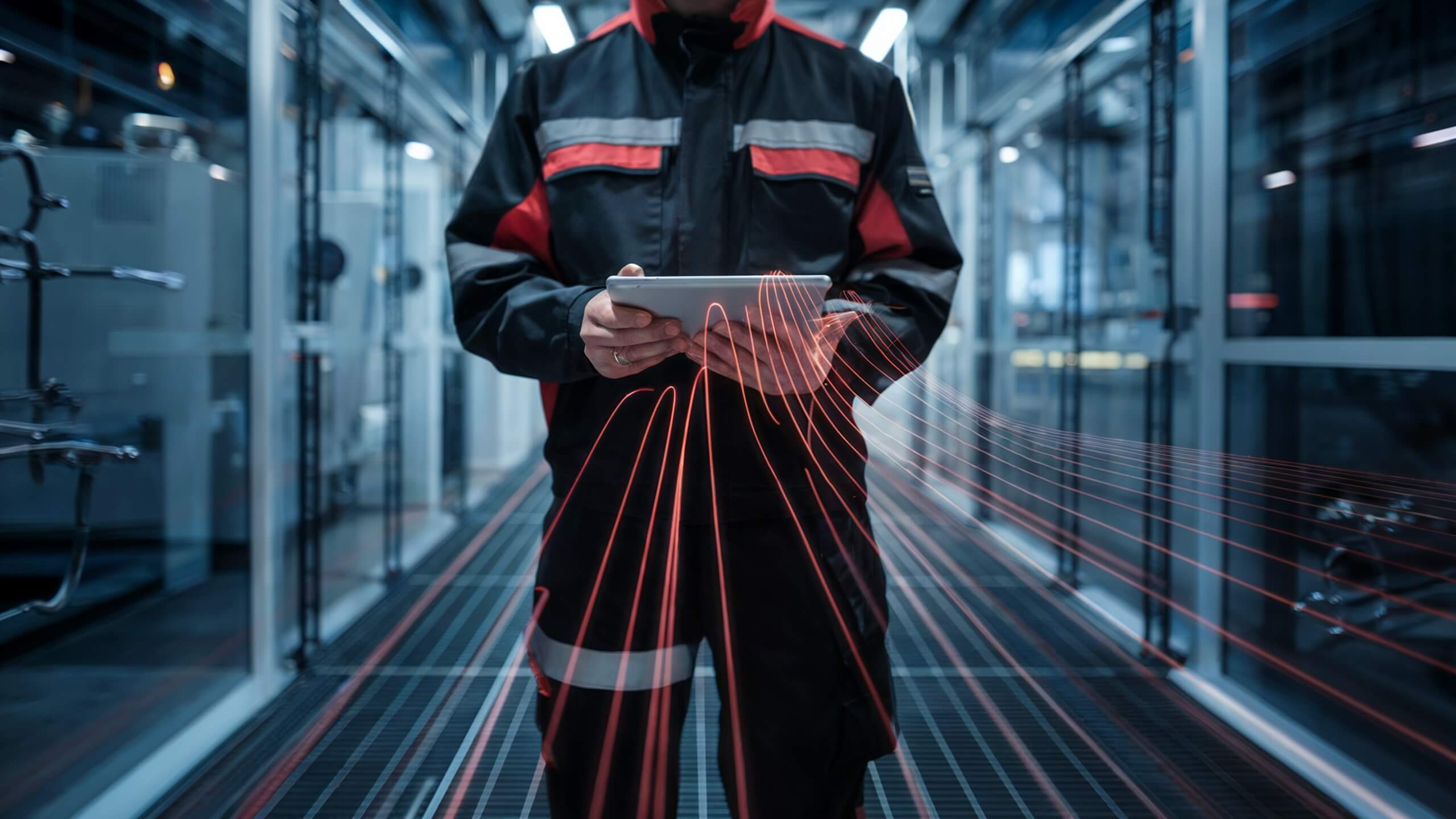 Technician in protective clothing standing in an industrial facility, operating a tablet, with red data lines representing digital technology and connectivity.